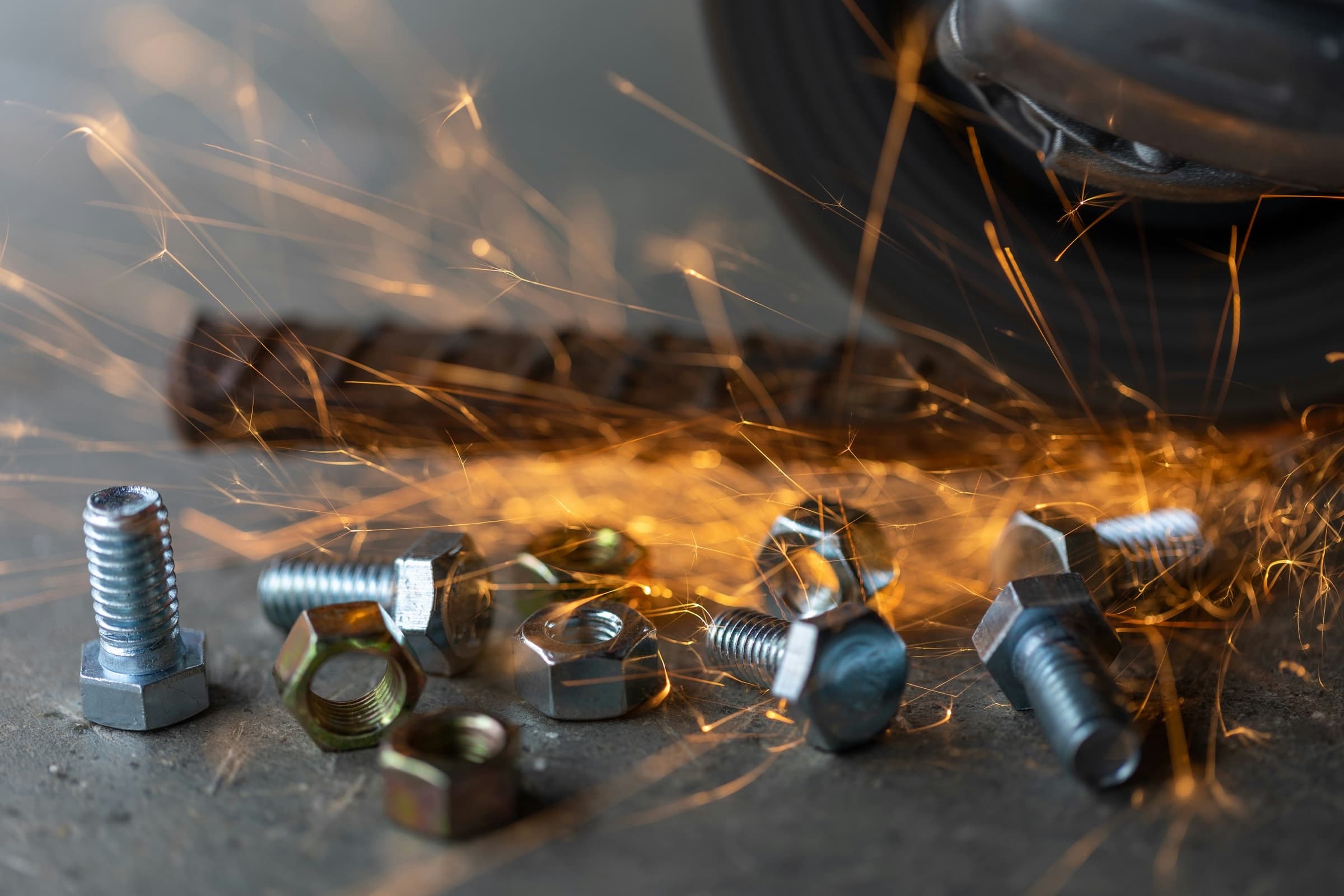 Scattered bolts, nuts, and hardware on a workbench with grinder sparks streaking through