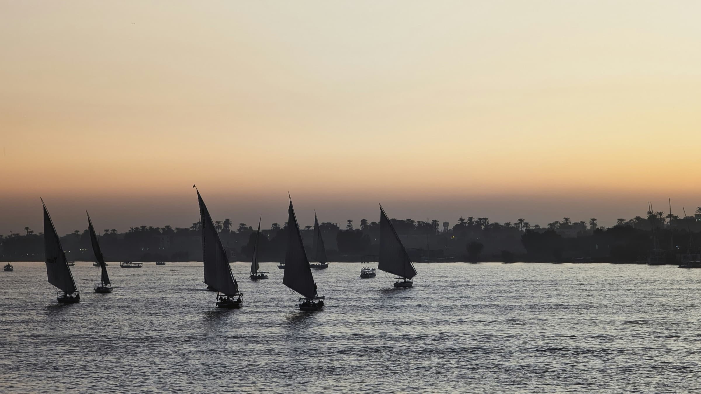Feluccas sailing on the Nile at dusk, silhouetted against a golden sky