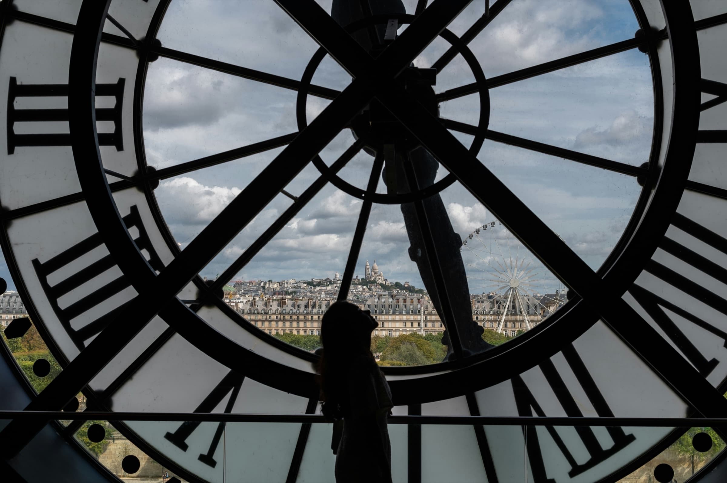 Silhouette of a woman looking through the Musée d'Orsay clock at Sacré-Coeur and the Paris skyline